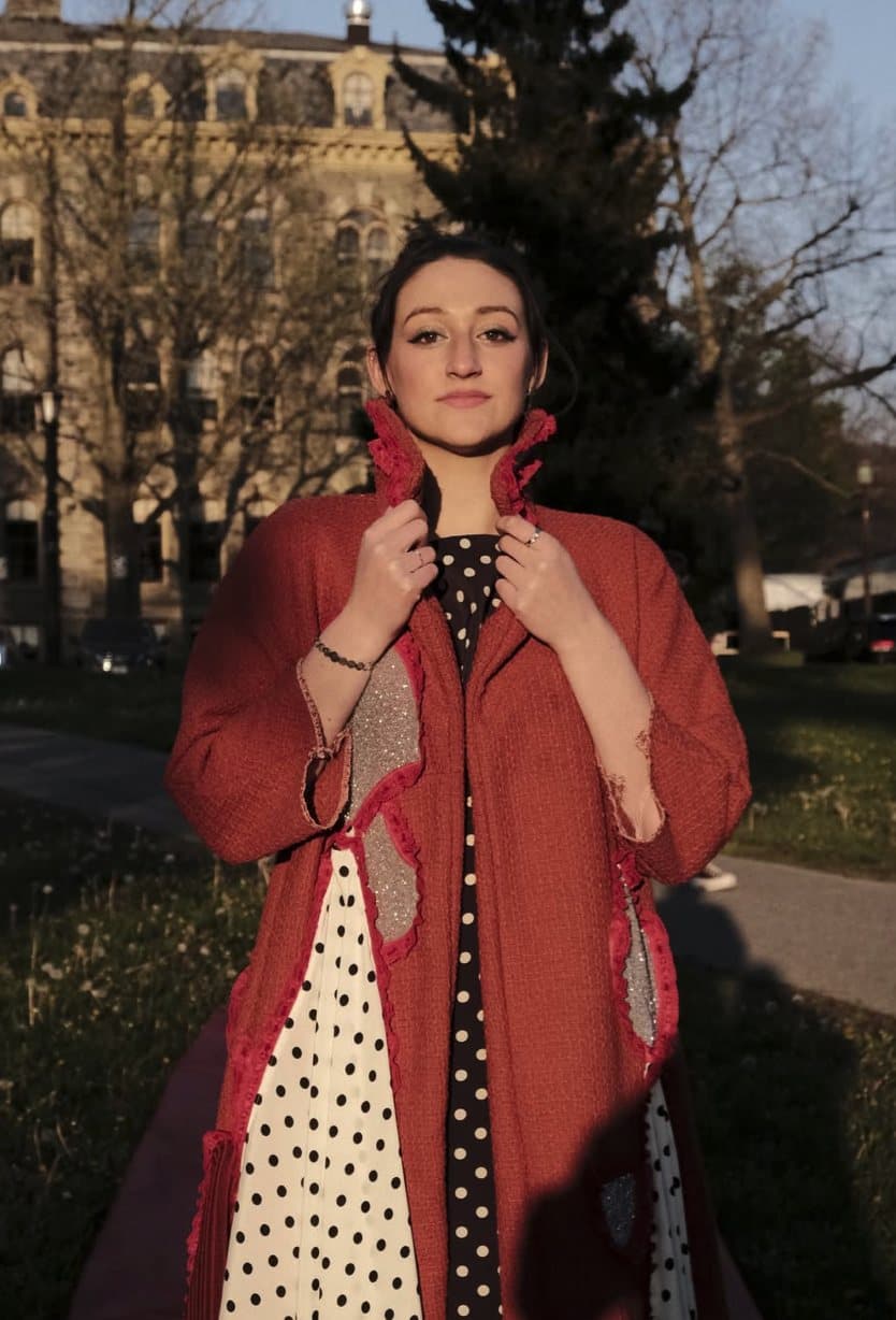 Remy on campus in a red textured coat with sparkly patches over a polka-dot dress