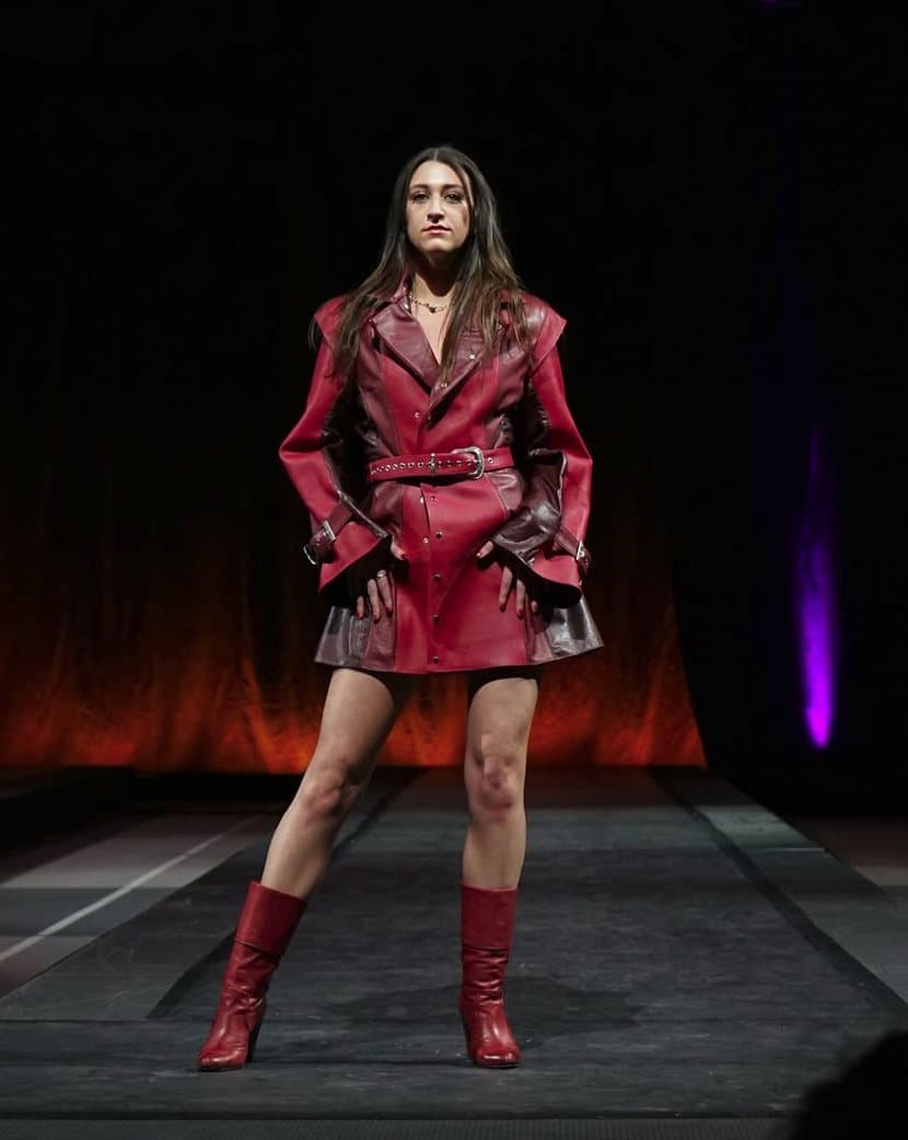 Remy on the runway at a Cornell Fashion Collective show in a red leather belted jacket and red boots