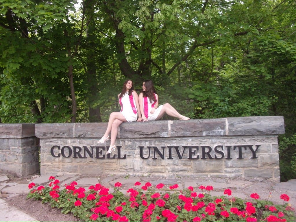 Remy and a friend in graduation stoles sitting on the Cornell University sign
